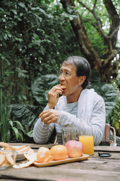 亚洲老人在户外剥橘子皮吃橘子做午餐。