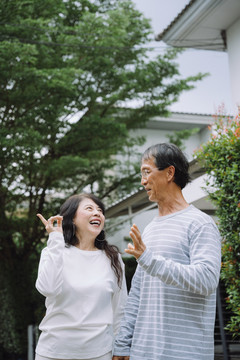 一对亚洲老夫妇一边在公园里散步一边看着飞鸟。