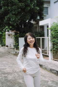 一位穿着白衬衫的快乐健康的亚洲老妇人早上在街上慢跑。