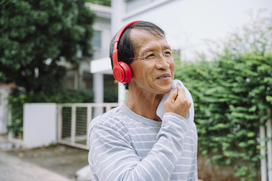 活跃的亚洲老人在公园跑步，用红色耳机听音乐。