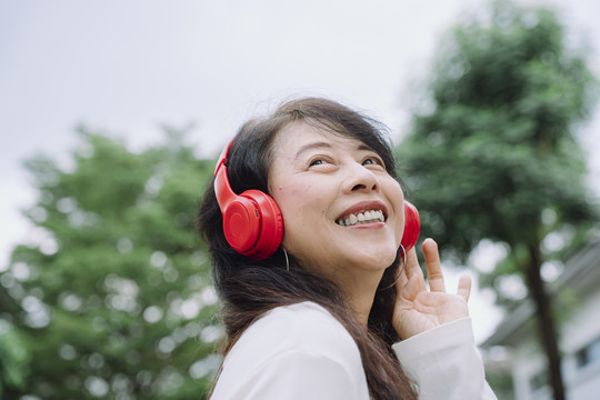 亚洲资深女性在公园用无线耳机听音乐的特写照片。