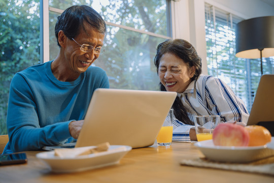 快乐的亚洲老年夫妇在家使用笔记本电脑上网。