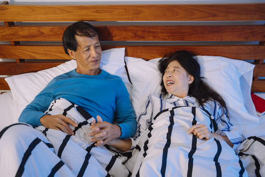 浪漫的亚洲老年夫妇晚上手牵手在床上。