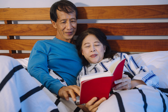 一对亚洲老年夫妇在卧室里一起看书。