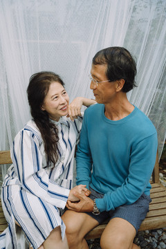 亚洲老年夫妇坐在木凳上手牵手的肖像。