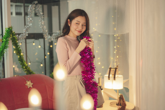 晚上，一位年轻的亚洲女士穿着粉色毛衣，用圣诞道具装饰她的房间。