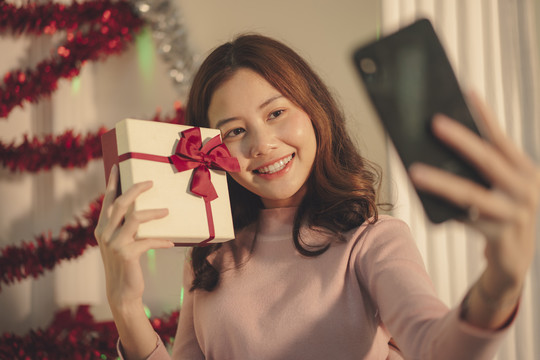 在圣诞派对上，年轻的亚洲女性正在用智能手机自拍或聊天。