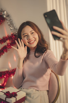 在圣诞派对上，年轻的亚洲女性正在用智能手机自拍或聊天。