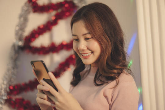 美丽的亚洲年轻女子在圣诞派对上快乐地玩着智能手机。