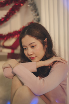 美丽的亚洲年轻女子，一头黑发，独自坐在聚会室里。独自一人过圣诞节。
