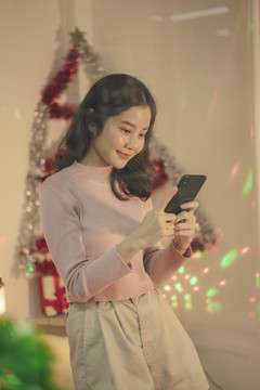 美丽的亚洲年轻女子黑发在圣诞派对上玩智能手机。