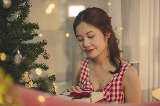 美丽的亚洲年轻女子黑发打开圣诞树下的礼品盒。