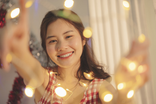特写镜头——美丽的亚洲年轻女子，黑头发，在家里玩圣诞灯。