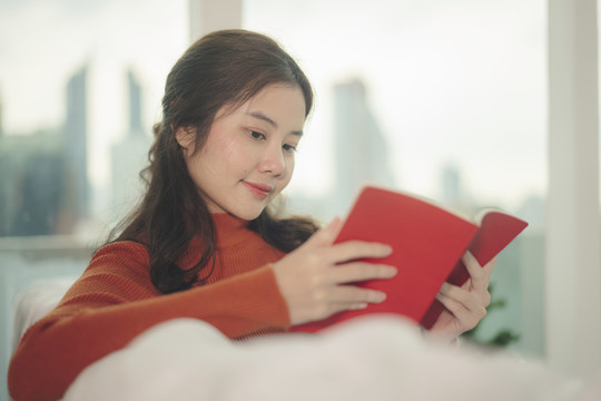 美丽的亚洲年轻女子黑发在家读红皮书。
