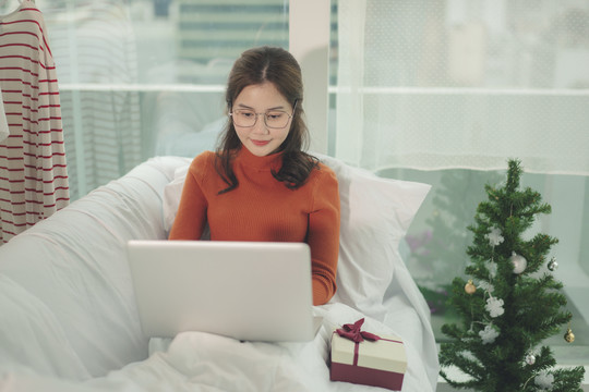 美丽的亚洲年轻女子戴着眼镜黑头发在圣诞节和朋友在笔记本电脑上聊天。