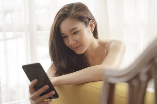 年轻亚洲美女在沙发上使用智能手机的特写照片。