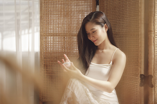 年轻的亚洲美女在家用护肤霜罐涂抹皮肤。