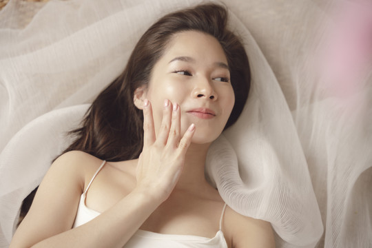 俯视图-年轻的亚洲美女在脸上涂抹乳液霜。