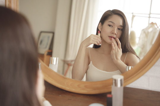 年轻的亚洲美女在化妆桌上涂唇膏。