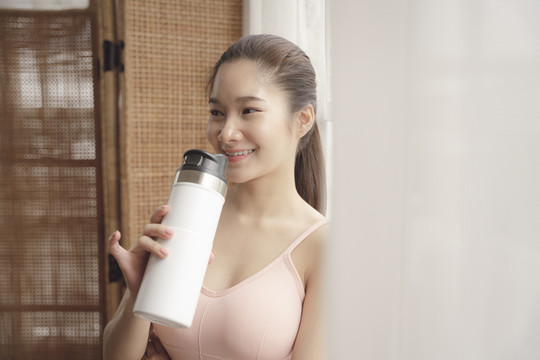 健康的亚洲年轻女性在锻炼后休息，喝瓶装水。