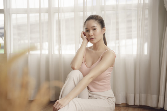 穿着粉红色衬衫坐在地板上的年轻亚洲美女肖像。