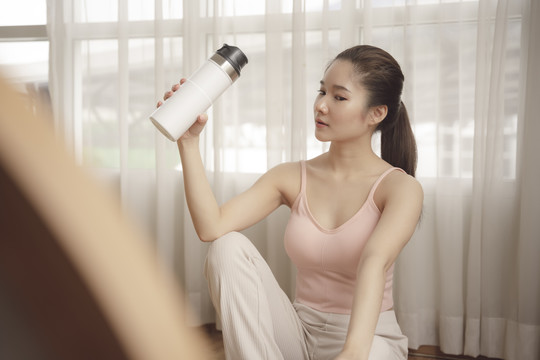 健康年轻的亚洲美女从瓶子里喝水。