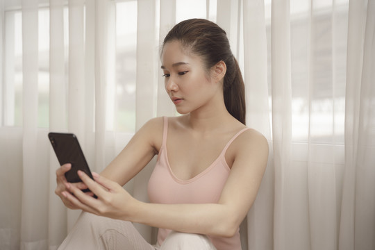 年轻的亚洲美女在家使用智能手机进行视频聊天或直播。