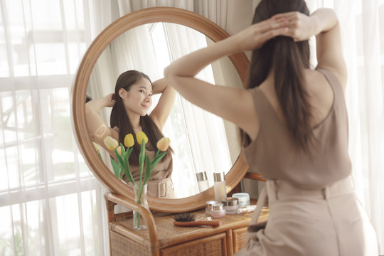 年轻的亚洲美女把头发系在圆镜前。