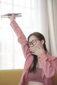年轻的亚洲美女书呆子女孩厌倦了看书，把手举在空中。