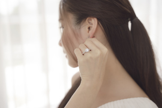 侧视图-年轻的亚洲美女戴着钻石戒指触摸左耳。