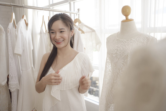 年轻的亚洲美女新娘在展厅挑选婚纱。
