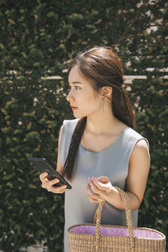 侧视图-年轻的亚洲美女手持智能手机购物。家庭主妇概念。