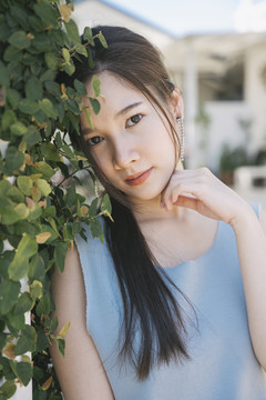 绿叶墙上穿着蓝色衬衫的年轻亚洲美女肖像。