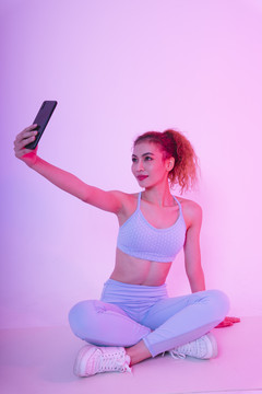 健康年轻的亚洲卷发女性在健身房使用智能手机的照片。
