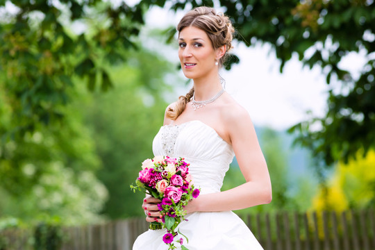 穿着婚纱的新娘在花园外佩戴新娘花束