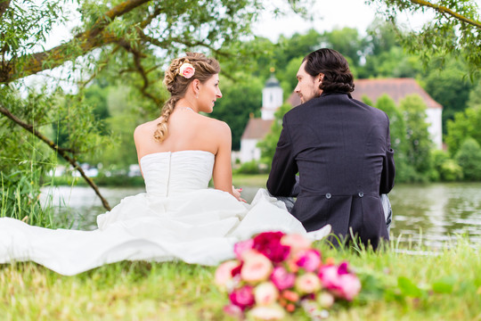 新娘和新郎的新婚夫妇坐在草地上，身后是新娘的花束，拍摄得很坦率