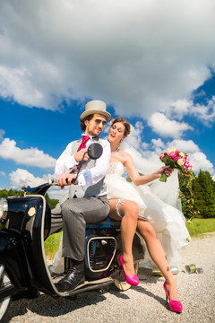 婚礼概念，新娘和新郎骑着摩托车，她正在展示腿上的吊袜带