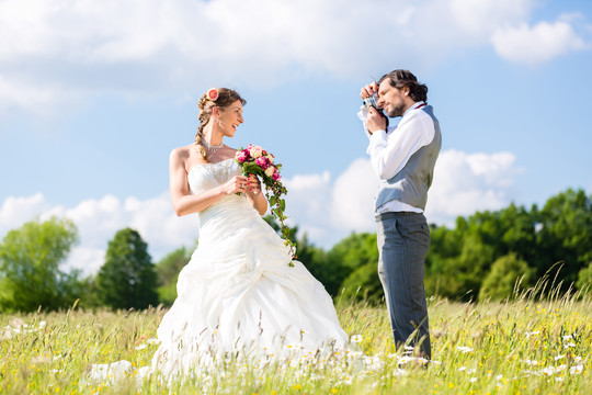 新郎在田野或草地上用相机拍摄新娘