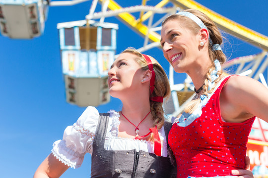朋友们穿着民族服装或在摩天轮前的迪恩德尔一起参观巴伐利亚博览会
