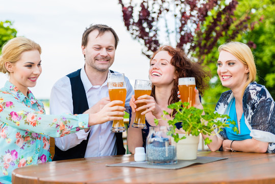 快乐的朋友们在花园餐厅用啤酒举杯