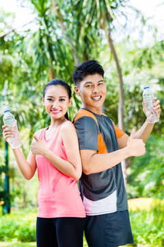 亚洲男女在公园健身训练后饮用水