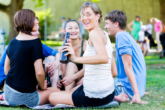 公园里的学生喝着啤酒，在河边野餐时聊天