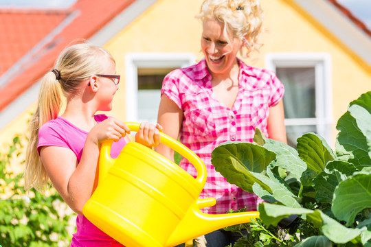 母亲和女儿在自家门前的花园里用罐子浇灌植物