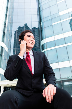 亚洲商人在塔楼前用智能手机打电话