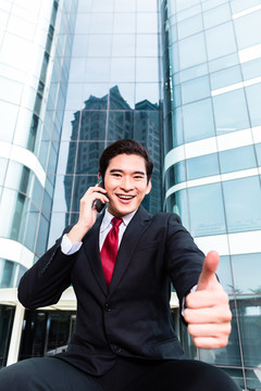 亚洲商人在塔楼前用智能手机打电话