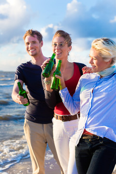 日落时分，朋友们在德国北海海滩上享用瓶装啤酒