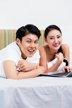 一对亚洲夫妇，一男一女，在卧室里用电脑上网