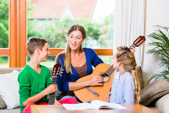 一家人在家用吉他演奏音乐，母亲、女儿和儿子一起演奏