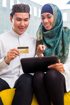 亚洲穆斯林男女在平板电脑上使用信用卡在线购物