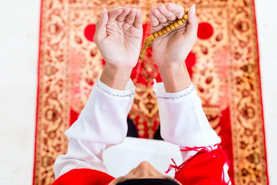 亚洲穆斯林妇女穿着传统服装，戴着珠链在地毯上祈祷